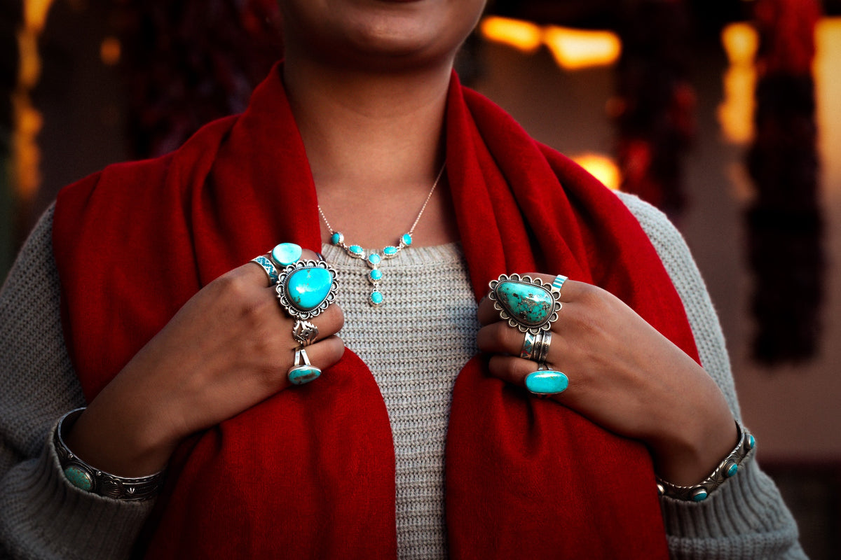 Hands wearing large turquoise and sterling silver rings and cuffs, holding a red scarf