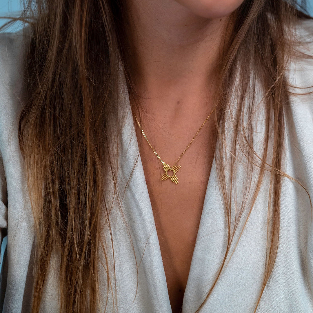 Enchantment: Petite Zia Pendant in sterling silver, worn on a gold chain, resting on a person's collarbone.