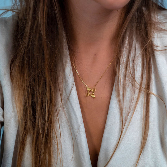 Enchantment: Petite Zia Pendant in sterling silver, worn on a gold chain, resting on a person's collarbone.