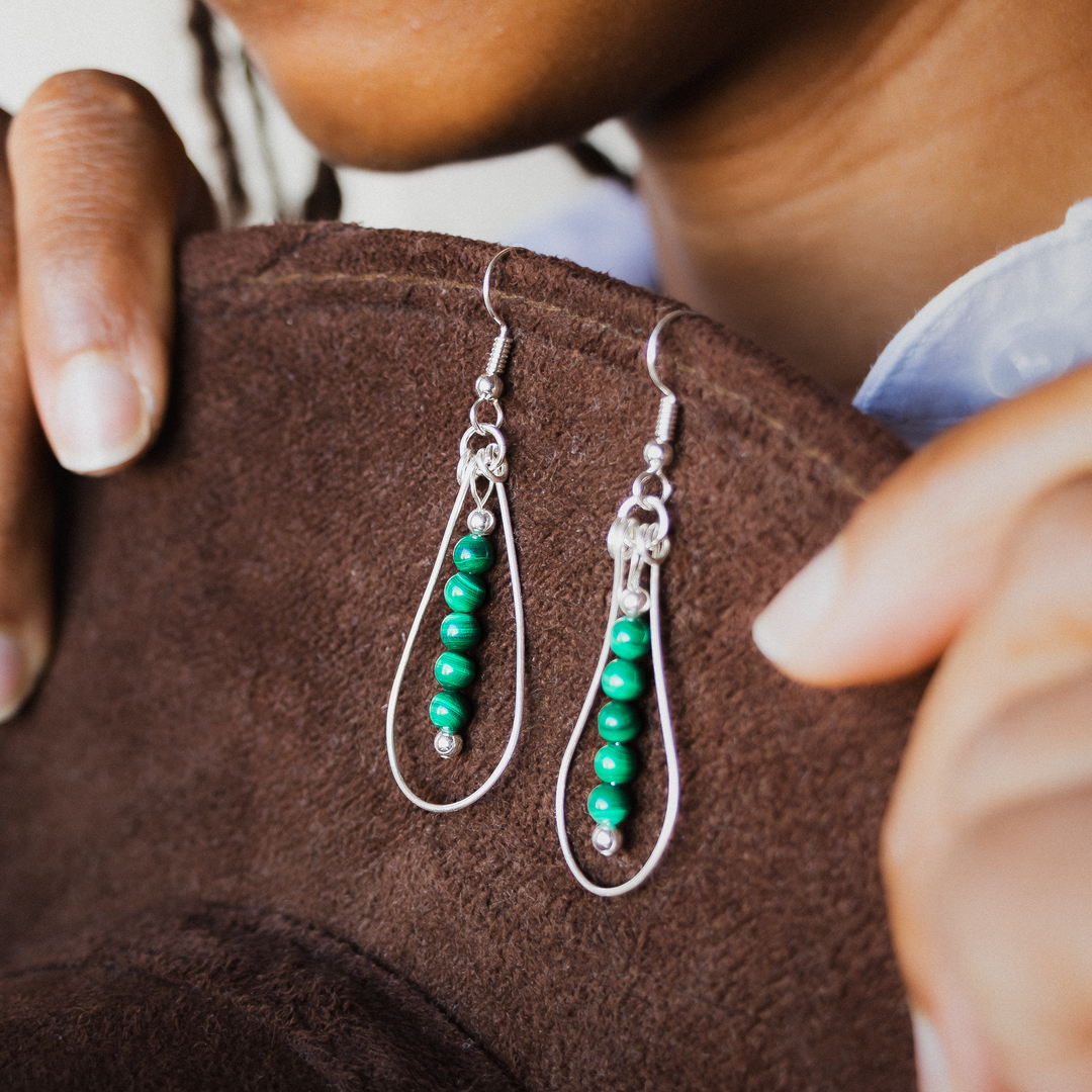 Bead Maiden: Wrapped Intention Earrings made of sterling silver with green beads, displayed against a brown background.
