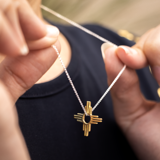 Enchantment: Petite Zia Pendant made of sterling silver with a gold accent, held by a person against a dark shirt.