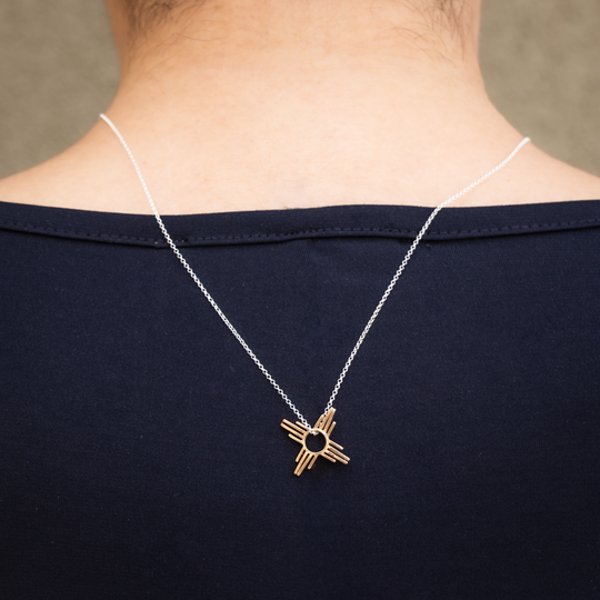Enchantment: Petite Zia Pendant in sterling silver, worn on a person's neck, showcasing its intricate design.