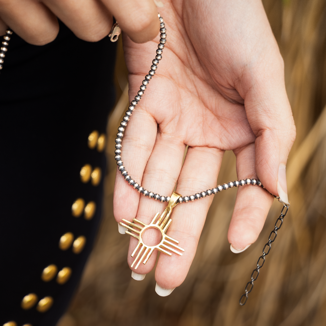 Enchantment: Zia Pendant with Silver Pearls, featuring a gold Zia symbol on a silver beaded chain.