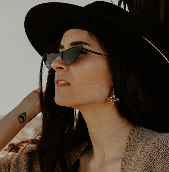 Enchantment: Zia Dangle Earrings in sterling silver, worn by a woman with long hair, sunglasses, and a hat.