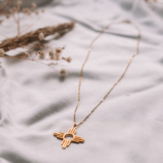 Enchantment: Zia Dangle Necklace in sterling silver, featuring a Zia symbol on a delicate chain, resting on soft fabric.