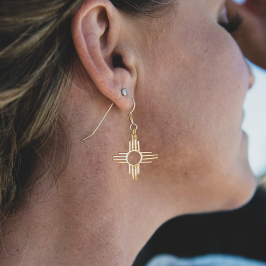 Enchantment: Zia Dangle Earrings in sterling silver, featuring a geometric Zia symbol design, worn on a model's ear.