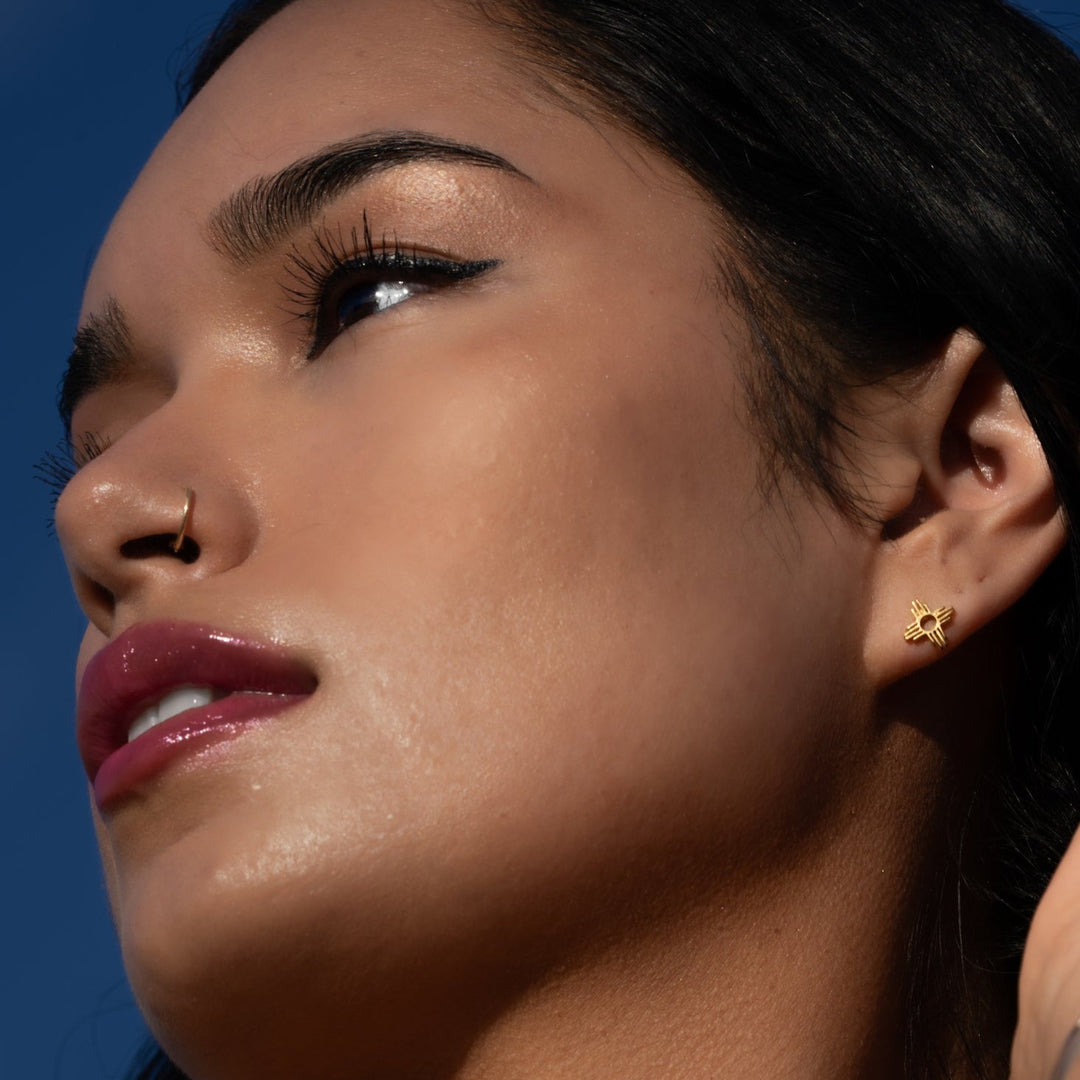 Enchantment: Petite Pendant & Zia Studs in sterling silver, showcased on a model's ear against a blue sky.