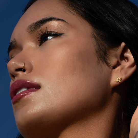 Enchantment: Petite Pendant & Zia Studs in sterling silver, showcased on a model's ear against a blue sky.