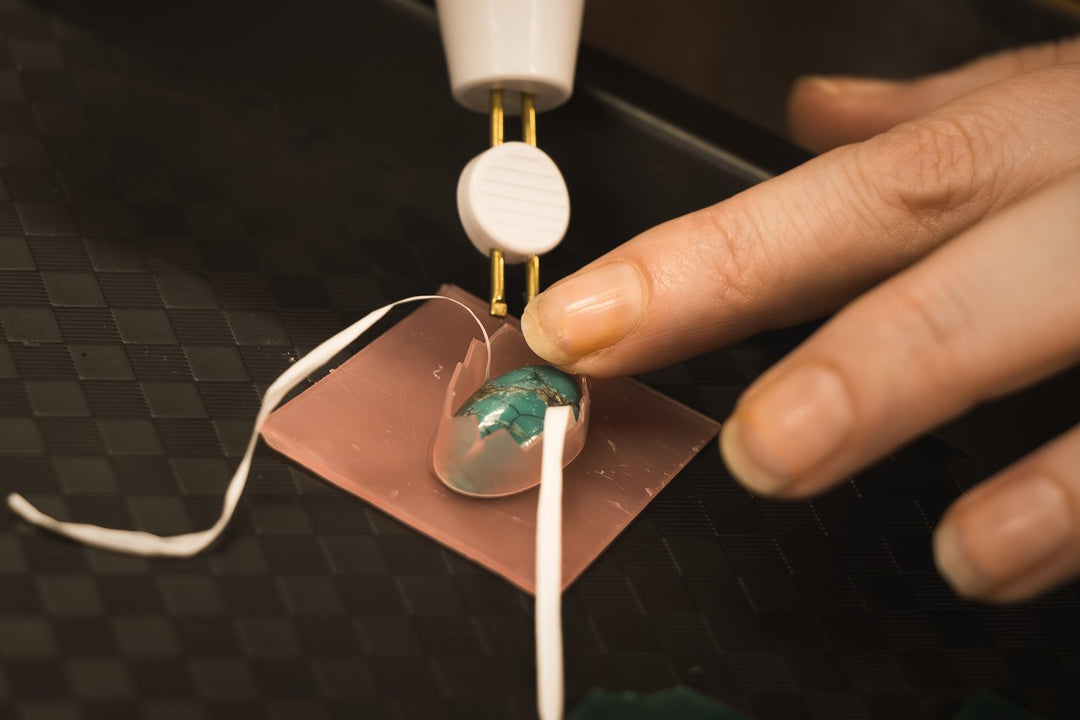Close-up of a stone-setting tool securing a piece of raw turquoise into a copper wax carving during a Craft & Cast session.